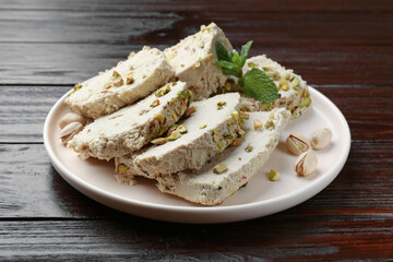 Pieces of tasty halva with pistachios and mint on wooden table, closeup