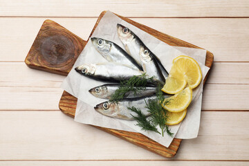 Fresh raw sprats, lemon and dill on light wooden table, top view