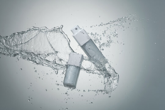 White cosmetic products with water splash on gray background.