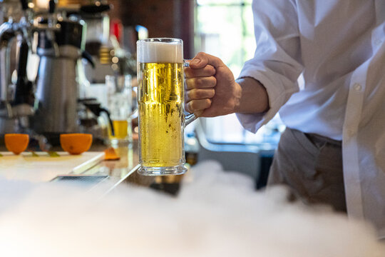 Anonymous bartender serve draft lager beer next to dry ice smoke 