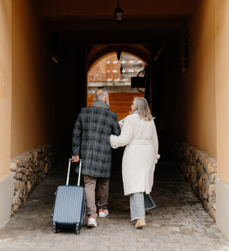 Elegant couple with suitcase in building arch
