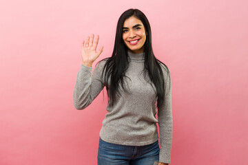 Gorgeous latin woman saying hi and waving looking happy
