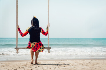 Traveler woman relaxing on swing above sea beach, summer holiday vacation trip