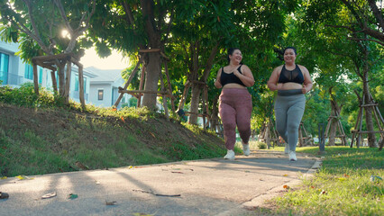 Fototapeta na wymiar Two asian woman fat in sportswear jogging together on pathway at park, woman and friends obesity doing activity with cardio or running, workout and exercise, plus size and health for weightloss.