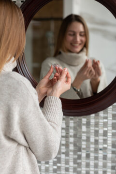 White girl puts on a clear braces while looking in the mirror