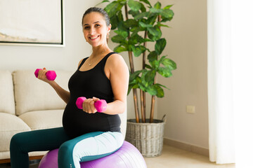 Fototapeta na wymiar Excited pregnant woman exercising with dumbbells and a fitness ball