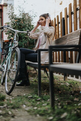 Casual young woman putting on headphones to enjoy music, sitting by a retro bicycle in an urban...