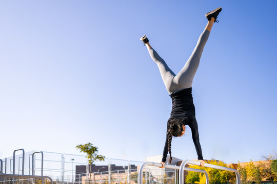 back view of fit woman doing handstand with splits on parallel bars