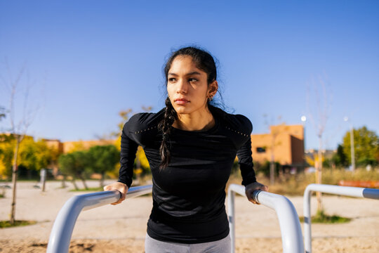 Focused sportswoman performing pull-ups on parallel bars