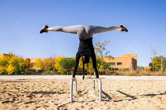  Fit female athlete performing handstand with splits on parallel bars