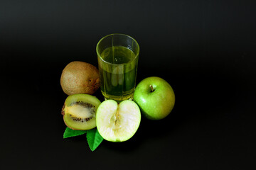 A tall glass of freshly squeezed fruit juice on a black background, next to ripe kiwi slices and a...