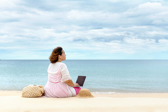 A woman using laptop computer while sitting on the beach