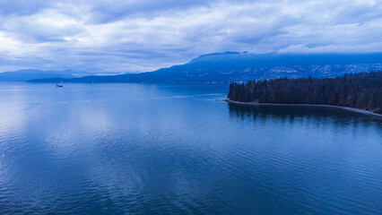 Edge of Stanley Park with West Vancouver and mountains in the background at sundown on a cloudy evening