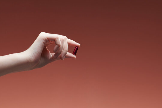 woman hand holding yellow pill capsule on red background