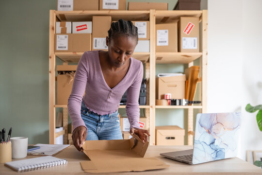 Focused black manager folding cardboard box on table