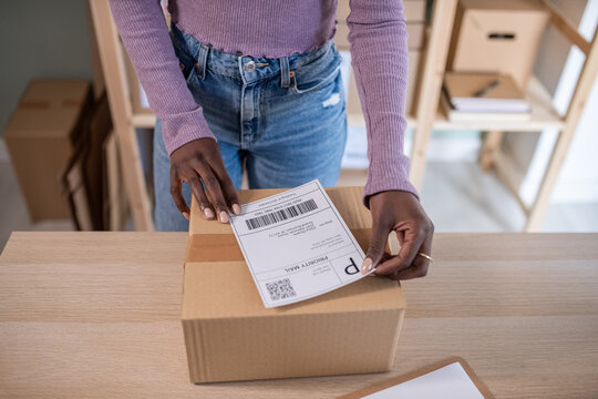 Crop black employee sticking label on parcel