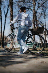 A woman in casual attire takes a break in a serene park with her vintage bicycle, showcasing a relaxed urban lifestyle moment.