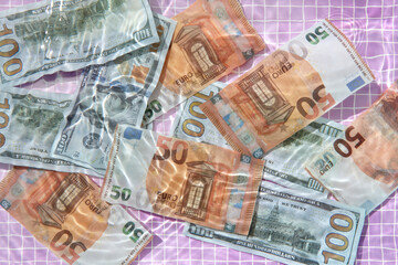 Euro and dollar bills underwater against pink pool tiles.