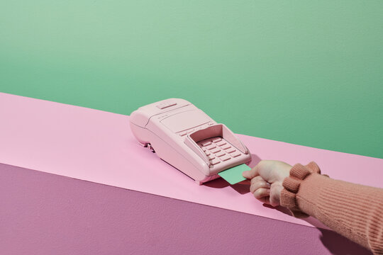 Woman using modern payment terminal on pink podium background