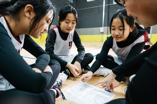 Teenager girls in basketball uniform looking at the strategy on floor