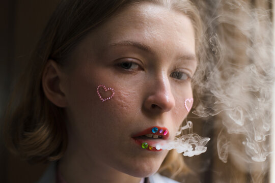 Woman with unconventional make up blowing smoke