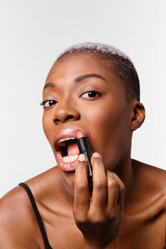 Woman applies lipstick while looking at the camera