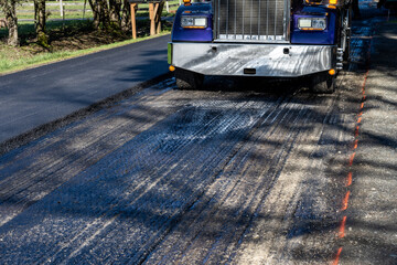 Road repaving project in progress, half the street repaved with fresh asphalt and half with front of dump truck loading hot asphalt into asphalt machine
