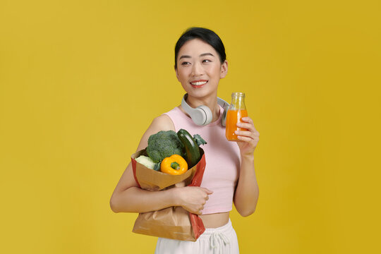 Young woman holds an orange smoothie and paper bag full of fruits