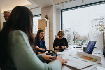 Colleagues in a light-filled office collaborate over documents, exemplifying teamwork and...