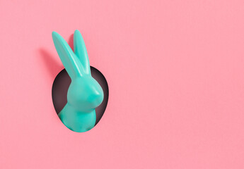 Creative composition with blue Easter bunny rabbit peeking out from hole on pink  background....