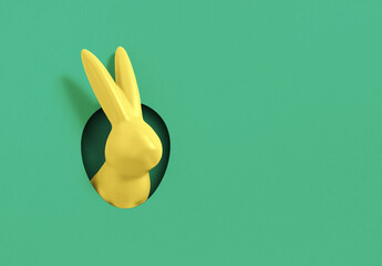 Creative composition with yellow Easter bunny rabbit peeking out from hole on green  background....
