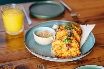 A plate of fried food with a side of dipping sauce sits on a wooden table