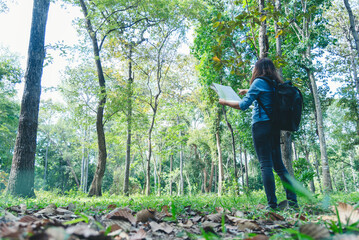 Naklejka na ściany i meble Women outdoor travel lifestyle Asian young woman traveler backpack looking map in green nature park. Female tourist backpacker holding brochure on vacation. Happy Tourism trip women journey walk park