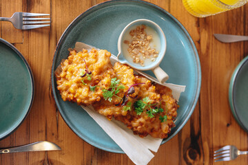 A plate of fried food with a side of sauce sits on a wooden table