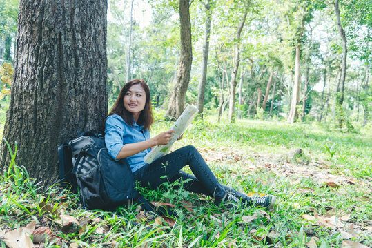 Women outdoor travel lifestyle Asian young woman traveler backpack looking map in green nature park. Female tourist backpacker holding brochure on vacation. Happy Tourism trip women journey walk park