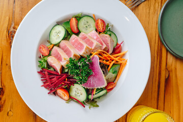 A white plate with a salad of vegetables and meat
