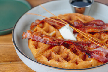 A plate of bacon and waffles with butter on top