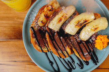 A plate of banana bread with chocolate sauce and a glass of orange juice