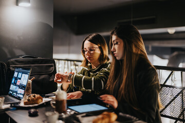 Two women working on a project together at a cozy evening cafe.