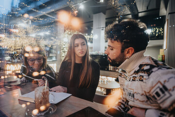 Young adults collaborating on a project at an evening cafe with festive lights.