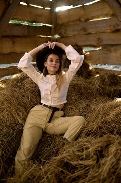 young blonde girl sitting on the hay in a wooden barn