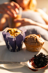 A woman is served coffee, muffins and jam in bed.