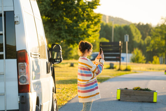 Woman standing near camper van and taking a picture with smartphone