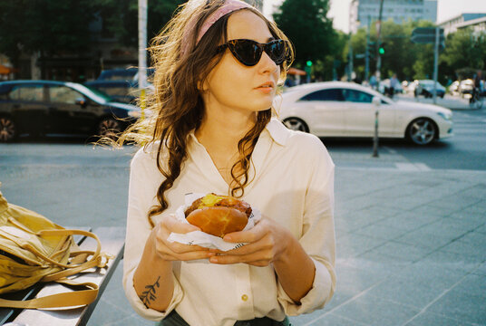 Woman eating burger on the background of the lively street
