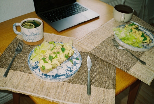 Two plates with breakfast, two cups of tea and laptop on the table
