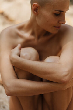 Graceful naked lady embracing knees in park