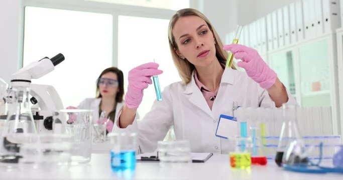 Woman chemist compares colors of two chemical liquids in test tubes