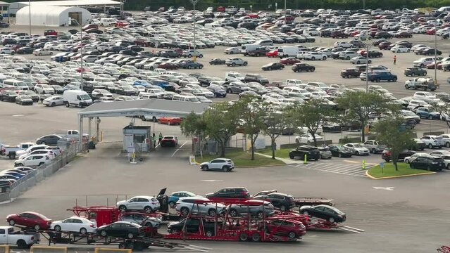 Big rig long haul semi truck tractors transporting used cars on two level modular semi trailers at auction dealer company big parking lot. Sales of secondhand vehicles