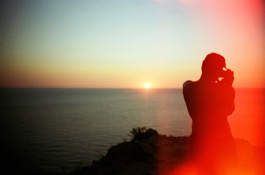 Silhouette of traveler taking picture of sunset in front of the sea