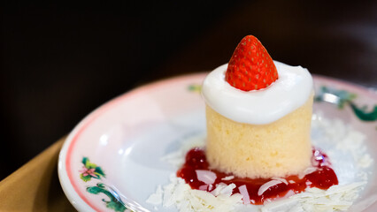 A single strawberry shortcake with whipped cream on a floral plate garnished with strawberry sauce and shredded coconut sweet dessert dish menu